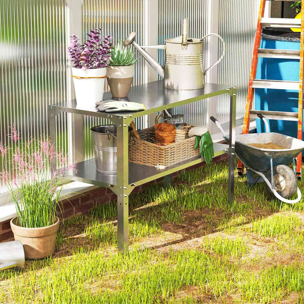 Table de rempotage argentée avec plantes, panier et arrosoir près d’une serre