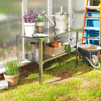 Table de rempotage argentée avec plantes, panier et arrosoir près d’une serre