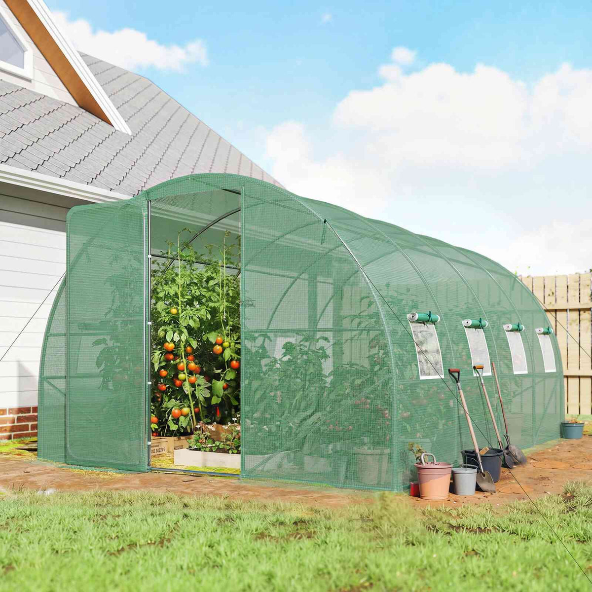 Serre tunnel verte contenant des plantes devant une maison
