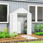 Petite serre blanche avec plantes sur étagères près d’une maison