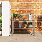 Table de rempotage garnie de plantes et d’un arrosoir contre un mur en briques