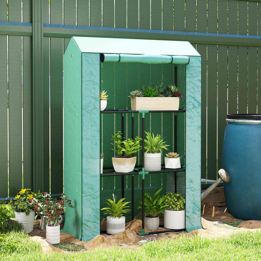 Mini serre verte avec plantes en pots devant une clôture