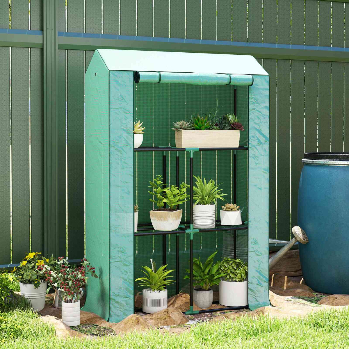 Mini serre verte avec plantes en pots devant une clôture