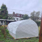 Serre tunnel blanche montée dans un potager entouré d’un grillage