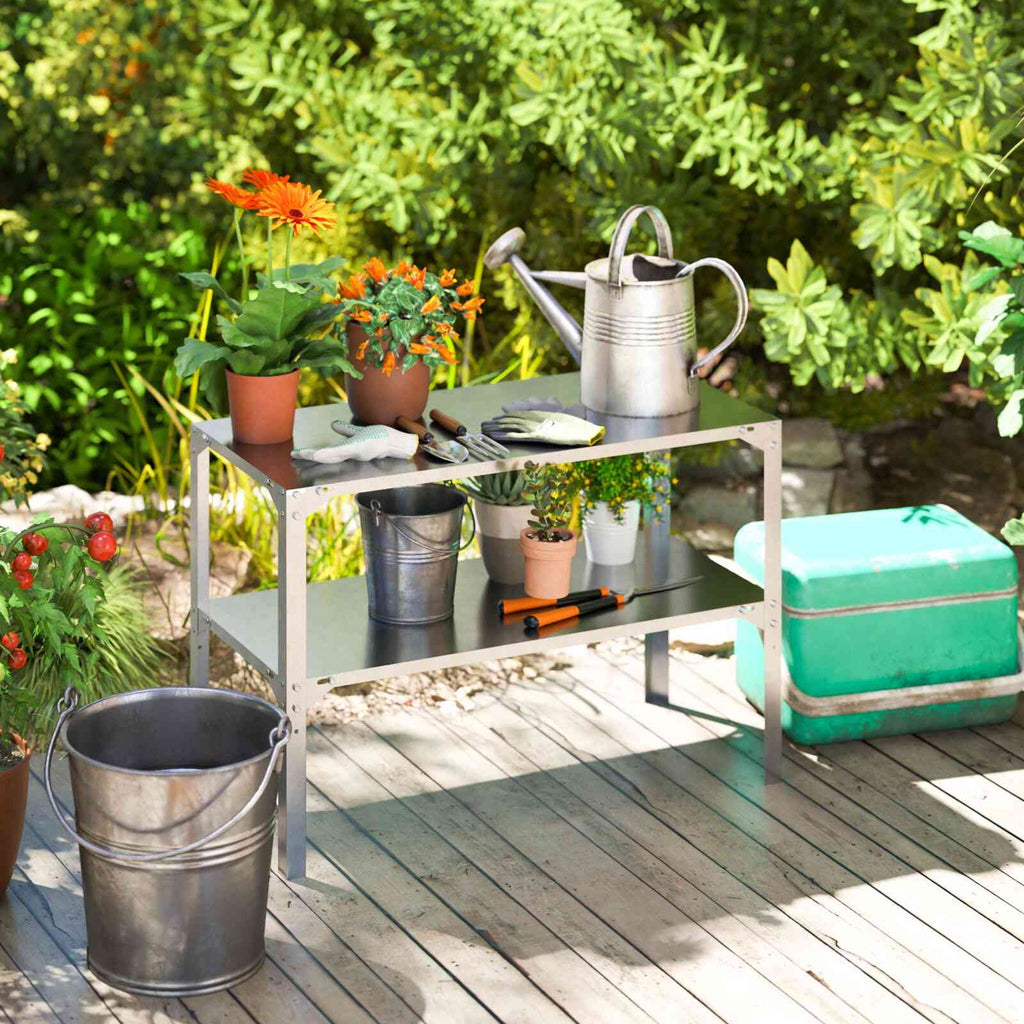 Table de rempotage avec plantes et arrosoir sur une terrasse entourée de verdure