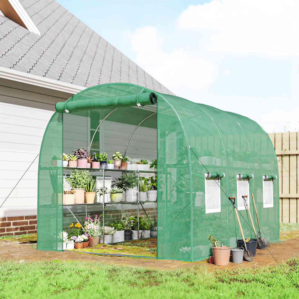 Serre tunnel verte avec étagères de plantes devant une maison