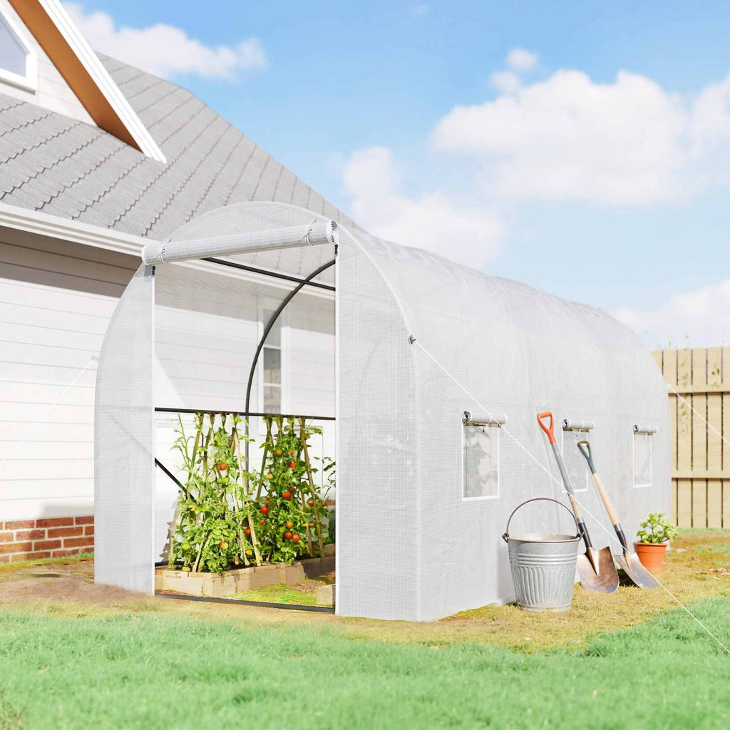 Serre tunnel blanche près d’une maison avec tomates à l’intérieur