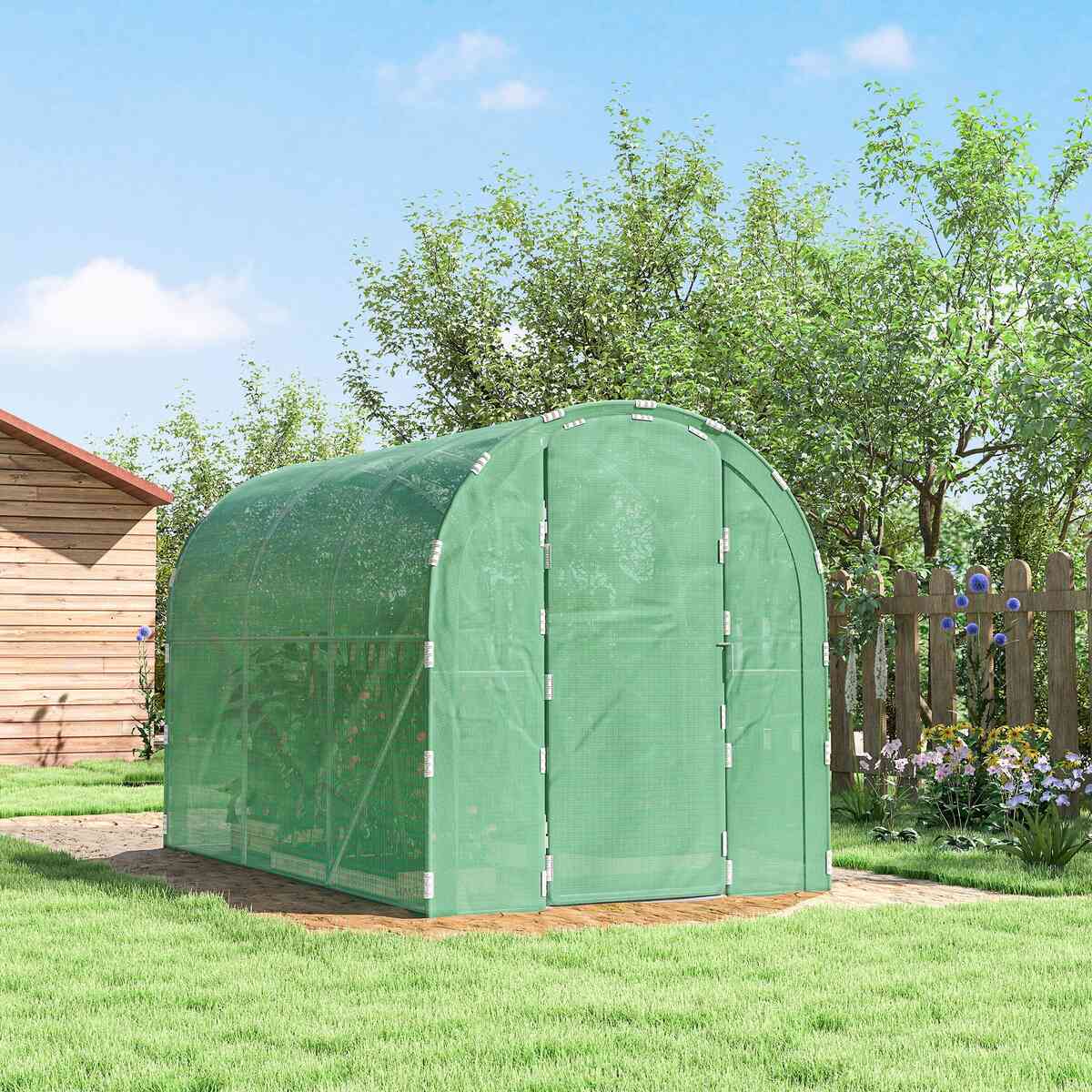 Serre tunnel verte fermée sur une pelouse près d’un abri de jardin