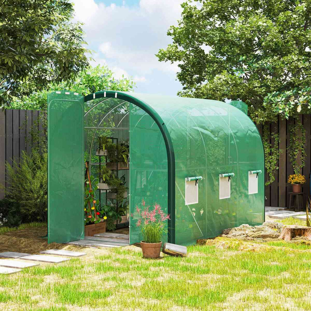 Serre tunnel verte ouverte avec plantes près de l’entrée au jardin