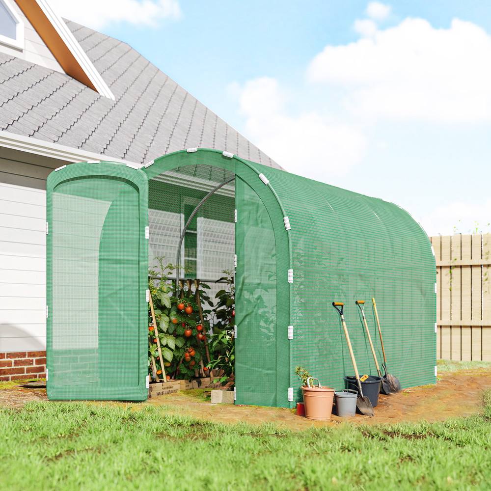 Serre tunnel verte contenant des tomates près d’une maison