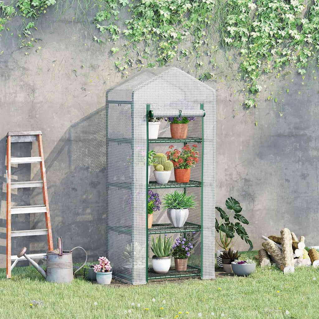 Serre à housse claire garnie de plantes contre un mur au jardin