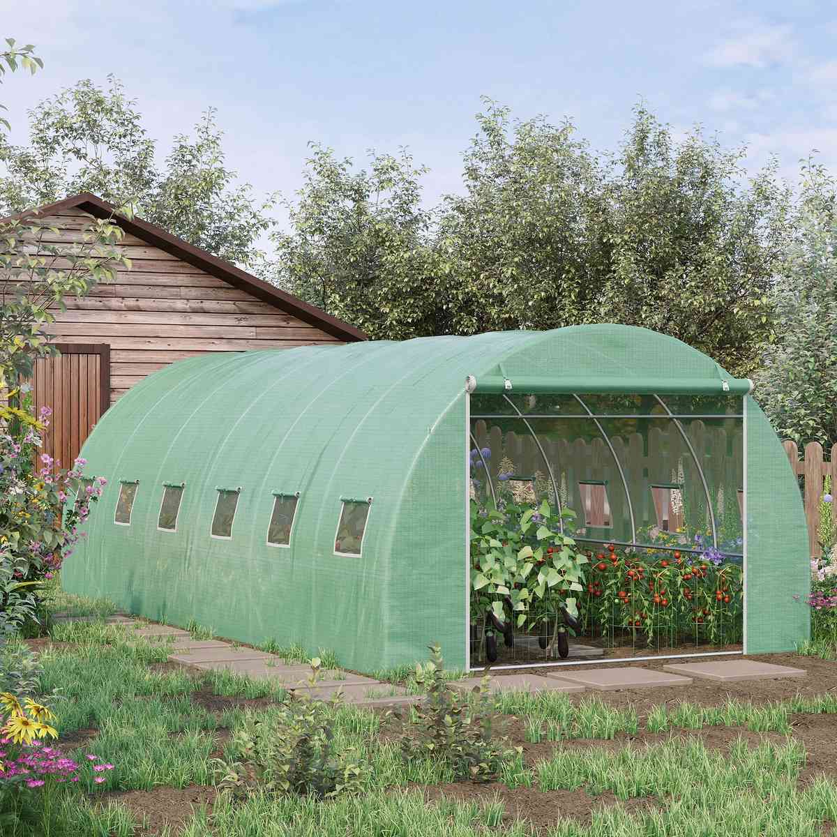Serre tunnel verte garnie de cultures devant un abri de jardin
