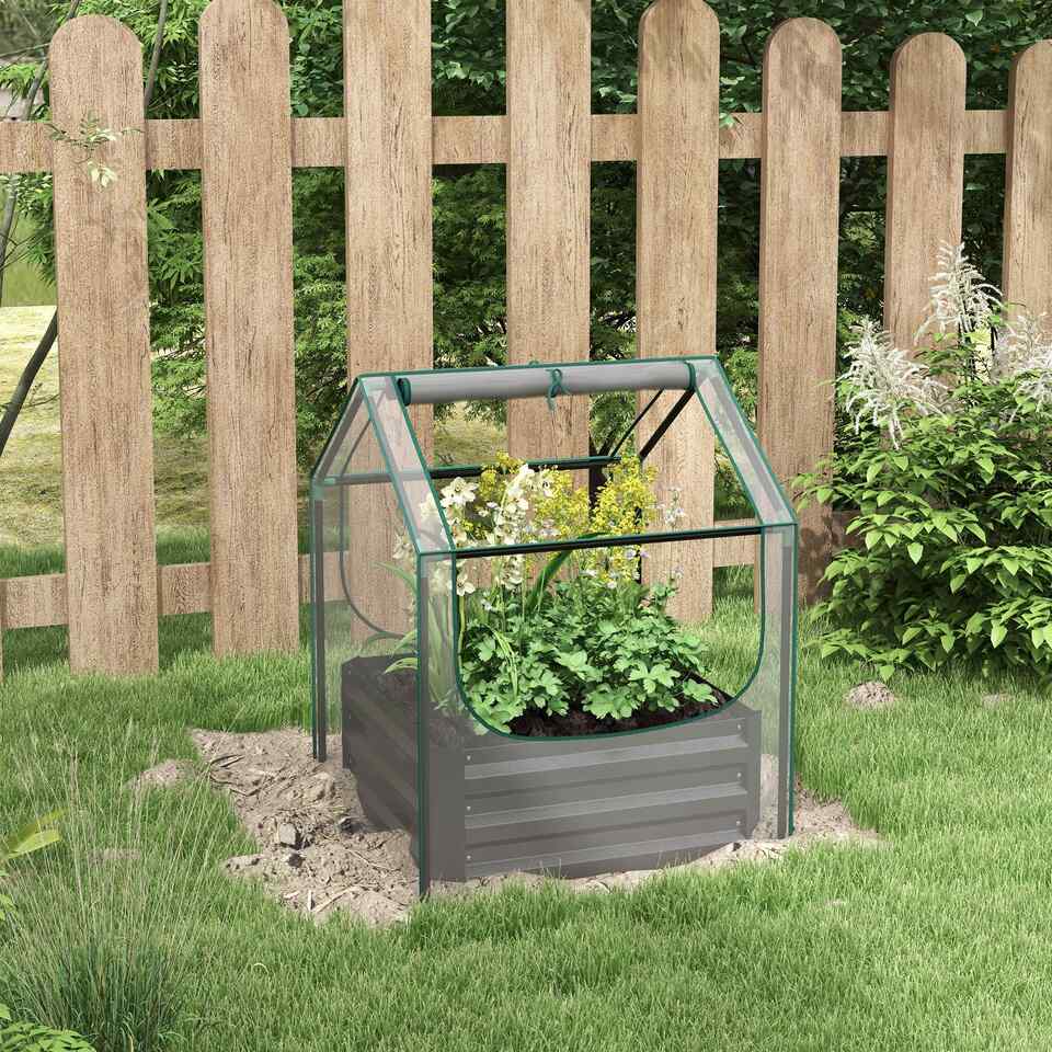 Carré potager gris avec housse transparente installé près d’une clôture en bois